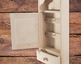 May include: A light wood key holder with a small drawer and a door that opens to reveal hooks for keys. The key holder is mounted on a wood wall.