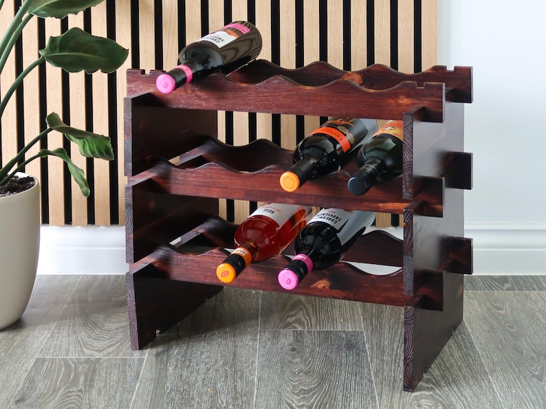 May include: A dark brown wooden wine rack with three shelves, each holding six bottles of wine. The rack is made of solid wood and has a rustic finish. The bottles are a mix of red and white wine.