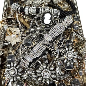 May include: A rectangular silver tray filled with a collection of costume jewellery, including rhinestone-encrusted bracelets, necklaces, a black and white cameo brooch, a butterfly-shaped pin, and various floral-shaped crystal accessories.