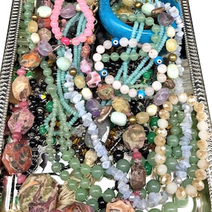 May include: A silver tray filled with a variety of beaded necklaces and bracelets. The jewelry includes pieces in shades of pink, green, blue, and black, with various stone and bead types. A turquoise bangle is also present.