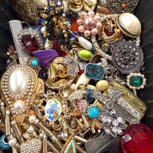 May include: A collection of vintage jewelry, including brooches, necklaces, and earrings. The assortment features various colors, including gold, silver, red, blue, and green. Many pieces have pearl and rhinestone accents, with floral and geometric designs.