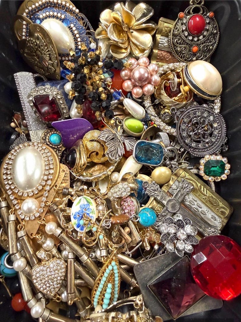 May include: A collection of vintage jewelry, including brooches, necklaces, and earrings. The assortment features various colors, including gold, silver, red, blue, and green. Many pieces have pearl and rhinestone accents, with floral and geometric designs.