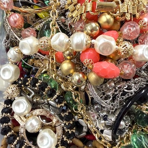 May include: A collection of vintage jewelry including necklaces, bracelets, and earrings. The jewelry features a variety of colors, including gold, silver, red, black, and white. The pieces are made of various materials, such as beads, metal, and plastic.