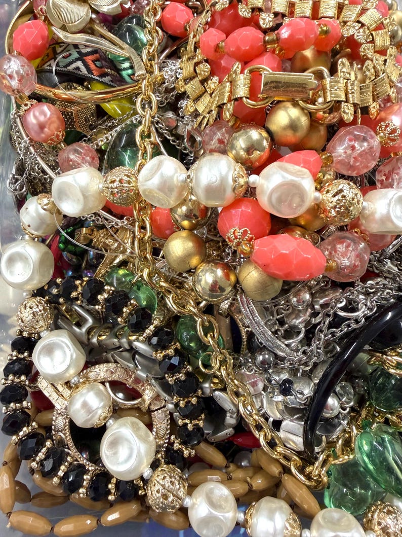 May include: A collection of vintage jewelry including necklaces, bracelets, and earrings. The jewelry features a variety of colors, including gold, silver, red, black, and white. The pieces are made of various materials, such as beads, metal, and plastic.