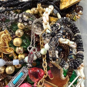May include: A collection of various necklaces, bracelets, and pendants. The jewelry includes gold, silver, and beaded pieces with accents of turquoise, pearls, and colorful gemstones. A gold-toned leaf pendant and a horse-shaped charm are visible.