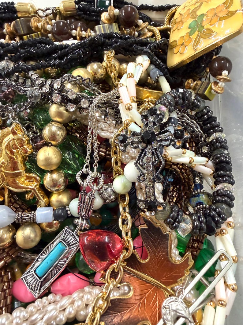 May include: A collection of various necklaces, bracelets, and pendants. The jewelry includes gold, silver, and beaded pieces with accents of turquoise, pearls, and colorful gemstones. A gold-toned leaf pendant and a horse-shaped charm are visible.