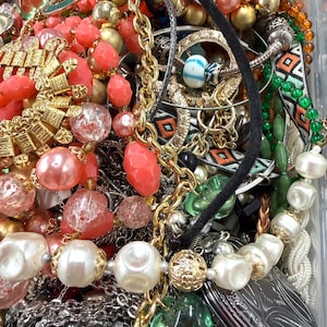 May include: A collection of vintage jewelry including necklaces, bracelets, and earrings. The pieces feature a variety of colors, including gold, silver, coral, and pearl. Some necklaces have large, round beads, while others have intricate chain designs.
