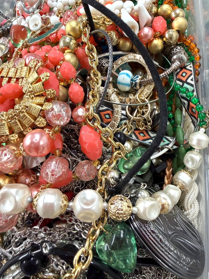 May include: A collection of vintage jewelry including necklaces, bracelets, and earrings. The pieces feature a variety of colors, including gold, silver, coral, and pearl. Some necklaces have large, round beads, while others have intricate chain designs.