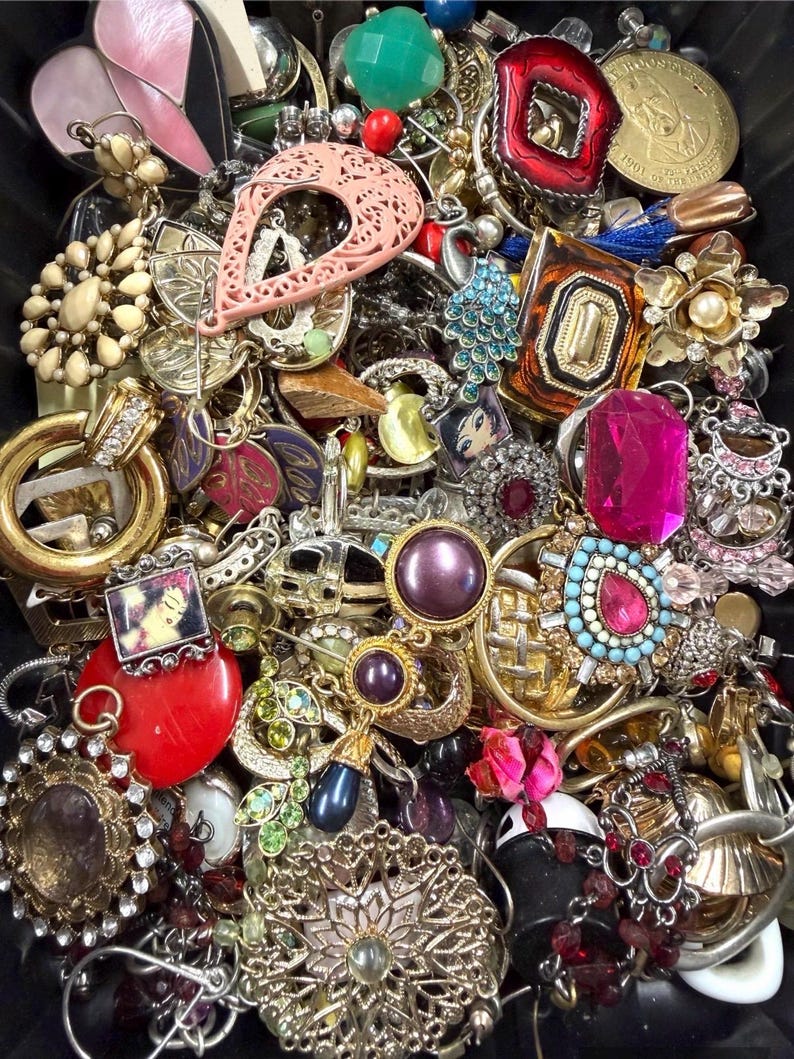 May include: A collection of vintage jewelry, including earrings, brooches, and pendants. The pieces feature various colors, shapes, and materials, such as gold, silver, red, pink, and turquoise. Some items have gemstones and intricate designs.