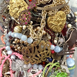 May include: A collection of various necklaces, bracelets, and pendants. The jewelry includes gold-toned heart-shaped pendants, beaded necklaces in shades of pink and blue, and a silver owl pendant. There are also chains and a gold monogram pendant.
