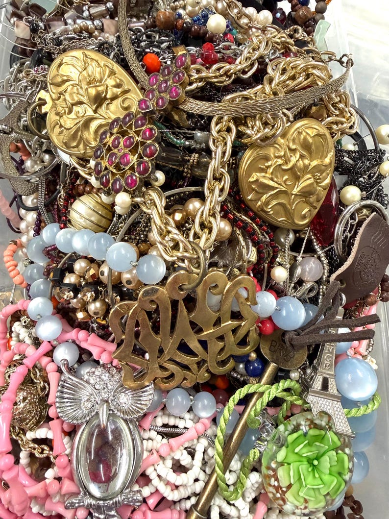 May include: A collection of various necklaces, bracelets, and pendants. The jewelry includes gold-toned heart-shaped pendants, beaded necklaces in shades of pink and blue, and a silver owl pendant. There are also chains and a gold monogram pendant.