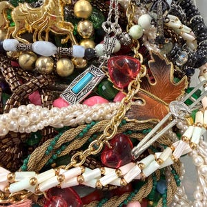 May include: A collection of vintage jewelry including necklaces, bracelets, and pendants. The assortment features gold-toned metal, faux pearls, and colorful beads. Notable pieces include a gold carousel horse pendant and heart-shaped charms.