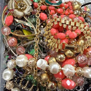 May include: A collection of vintage jewelry including necklaces, bracelets, and earrings. The pieces feature a variety of colors, including gold, coral, white, and black. Some items have floral and geometric designs, with pearls and beads.
