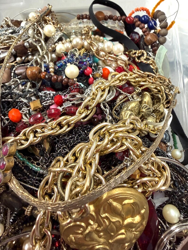 May include: A close-up shot of a collection of assorted jewelry, including necklaces, bracelets, and beads. The jewelry features a variety of colors, including gold, silver, red, and black. There are chunky gold chains, pearl necklaces, and beaded bracelets.