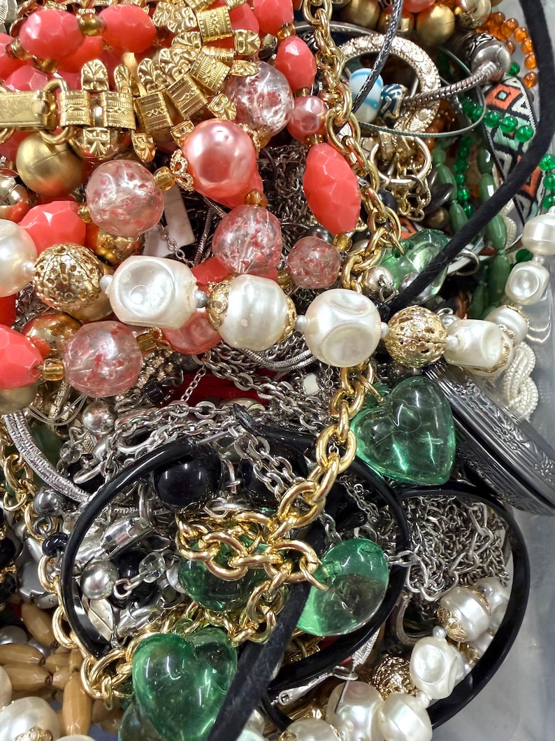 May include: A collection of assorted necklaces and jewelry. The image features gold, silver, and black chains, along with beads in shades of red, pink, white, and green. Some necklaces have heart-shaped pendants.