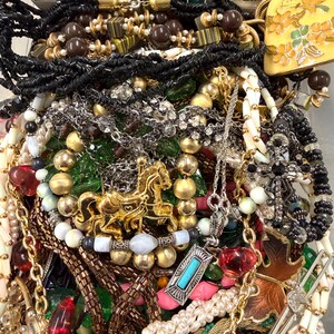May include: A collection of various necklaces and pendants in a variety of styles and colors. The jewelry includes beaded necklaces, chains, and pendants with gemstones and charms. Gold, silver, black, and white are the dominant colors.