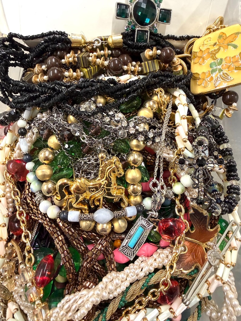 May include: A collection of various necklaces and pendants in a variety of styles and colors. The jewelry includes beaded necklaces, chains, and pendants with gemstones and charms. Gold, silver, black, and white are the dominant colors.