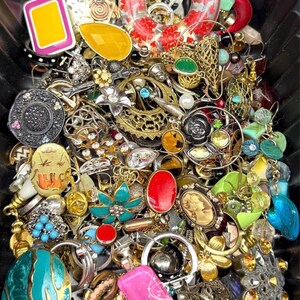 May include: A collection of vintage jewelry, including earrings, brooches, and rings, in various colors and styles. The assortment features gold, silver, red, turquoise, and yellow pieces with floral, geometric, and cameo designs. The jewelry is densely packed together.