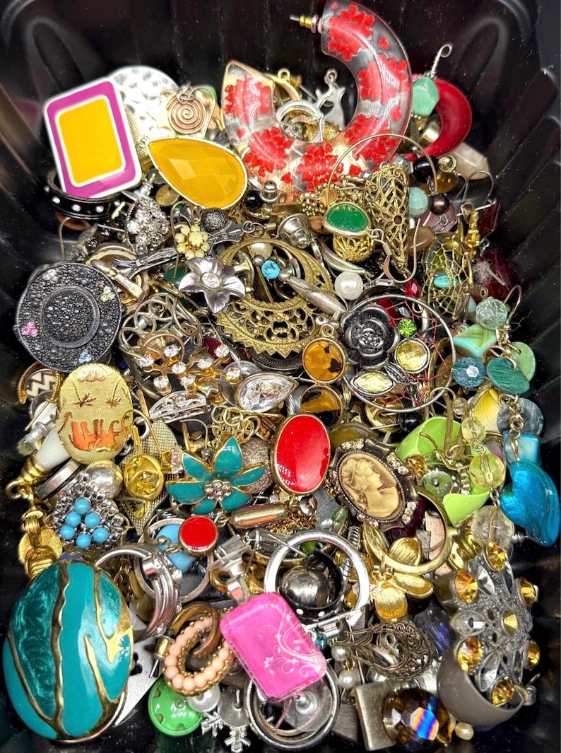 May include: A collection of vintage jewelry, including earrings, brooches, and rings, in various colors and styles. The assortment features gold, silver, red, turquoise, and yellow pieces with floral, geometric, and cameo designs. The jewelry is densely packed together.