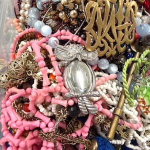 May include: A collection of vintage jewelry including necklaces, bracelets, and brooches. The assortment features pink coral beads, pearl strands, and a silver owl pendant. Gold-toned metal accents and blue beads add contrast to the mix.