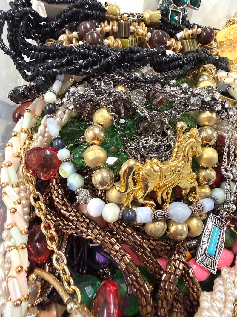 May include: A collection of various necklaces and jewelry pieces. The image features gold, silver, and beaded necklaces, along with pendants and bracelets. Colors include gold, silver, black, red, and white.