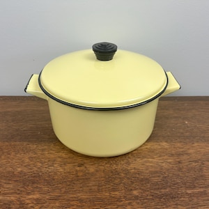 May include: A yellow enamel pot with a black lid and handle. The pot has a black rim around the top.