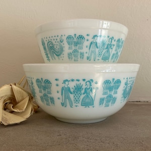 Puede incluir: Dos tazones de mezclar blancos con un diseño de arte popular azul y blanco. Los tazones están apilados uno encima del otro.