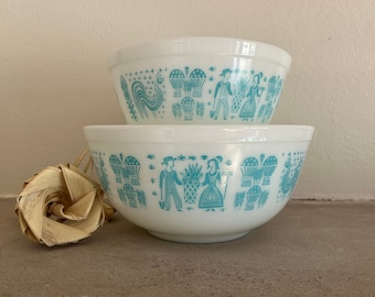 May include: Two white mixing bowls with a blue and white folk art design. The bowls are stacked on top of each other.