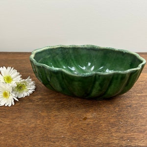 May include: A green ceramic bowl with a wavy, leaf-like design. The bowl is sitting on a wooden surface.