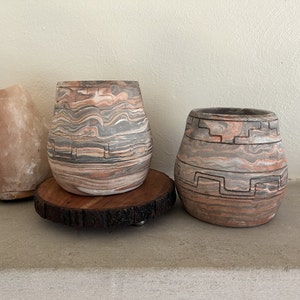 Puede incluir: Dos macetas de cerámica con un diseño marmoleado. Las macetas son marrones, grises y blancas con un patrón geométrico. Las macetas están sobre una superficie de madera.