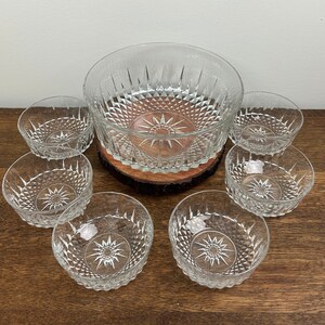 May include: A set of seven clear glass bowls with a diamond pattern. The bowls are arranged in a circle around a wooden base. The largest bowl is a salad bowl.