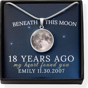 May include: A silver necklace with a round pendant featuring a detailed image of the moon. The pendant hangs from a silver chain, presented in a black box with text that reads "Beneath This Moon" and "18 Years Ago my heart found you".