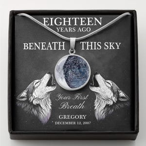 May include: A silver necklace with a circular pendant featuring a celestial design. The pendant is suspended from a chain and is presented in a black box. The text on the box reads "EIGHTEEN YEARS AGO BENEATH THIS SKY". The box also features two howling wolf illustrations.