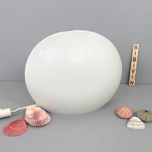 May include: A white spherical lamp with a textured surface, a power cord, and a switch. Several seashells in shades of pink, red, and beige are arranged near the lamp. The word "BIBIVIN" is spelled out with wooden letter blocks.