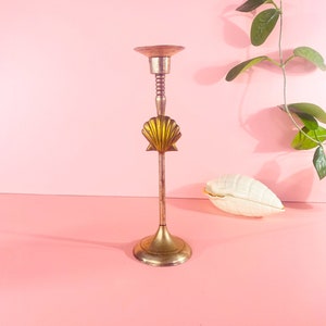 Puede incluir: Un candelero de metal dorado con un diseño de concha. El candelero tiene una base redonda y un tallo alto y delgado.