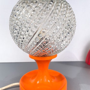 May include: A vintage orange table lamp with a clear glass globe shade. The globe has a textured, swirling pattern.