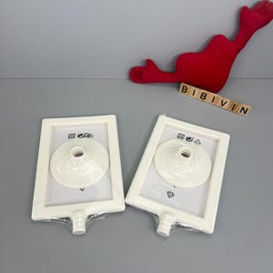 May include: Two white picture frames with a circular stand are displayed. The frames are rectangular with a circular stand in the center. The frames are packaged in clear plastic. The word "BIBIVIN" is spelled out with wooden letter tiles.