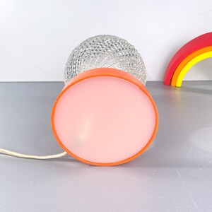 May include: A vintage table lamp with a clear glass globe shade and a pink and orange base. The lamp has a white cord.