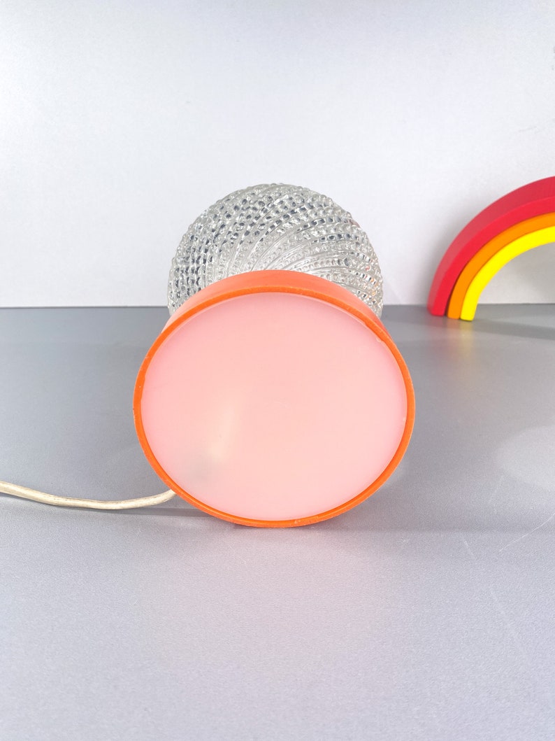May include: A vintage table lamp with a clear glass globe shade and a pink and orange base. The lamp has a white cord.