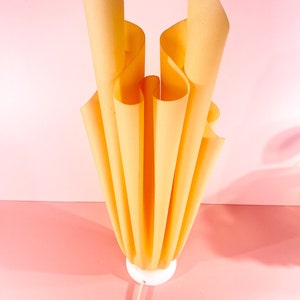 May include: A yellow, pleated lampshade with a white base. The lampshade is made of fabric and has a unique, organic shape.
