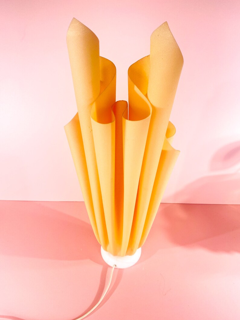 May include: A yellow, pleated lampshade with a white base. The lampshade is made of fabric and has a unique, organic shape.