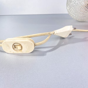 May include: A white electrical cord with a white inline switch and a white plug. The cord is coiled and the plug is unplugged.
