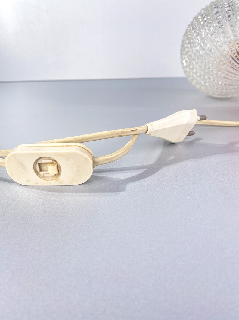 May include: A white electrical cord with a white inline switch and a white plug. The cord is coiled and the plug is unplugged.
