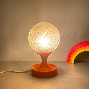 May include: A vintage orange and clear glass table lamp with a textured globe shade. The lamp has a round base and a cord.