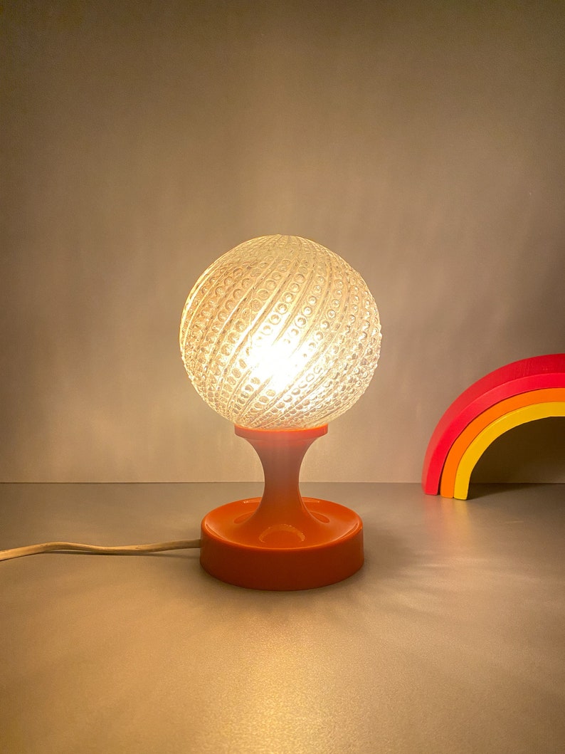 May include: A vintage orange and clear glass table lamp with a textured globe shade. The lamp has a round base and a cord.
