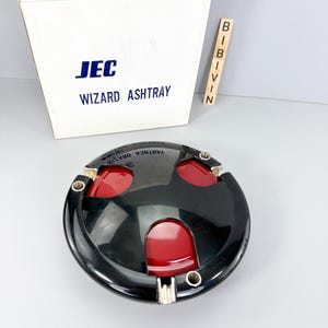 May include: Black and red round ashtray with the text "WIZARD ASHTRAY" on the box. The ashtray has three red compartments and a silver rim.