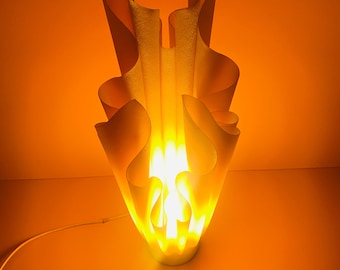 May include: A white, abstract, sculptural lamp with a warm, yellow light emanating from the center. The lamp is shaped like a flame and has a modern, minimalist design.