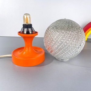 May include: Orange and white table lamp with a clear glass globe shade. The shade has a textured pattern of small bumps.