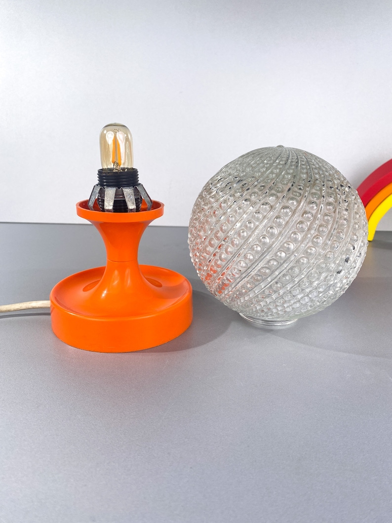 May include: Orange and white table lamp with a clear glass globe shade. The shade has a textured pattern of small bumps.
