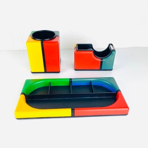 May include: A colorful desk organizer set with a black base and compartments in red, yellow, green, and blue. The set includes a pen holder, a tape dispenser, and a tray with multiple compartments.